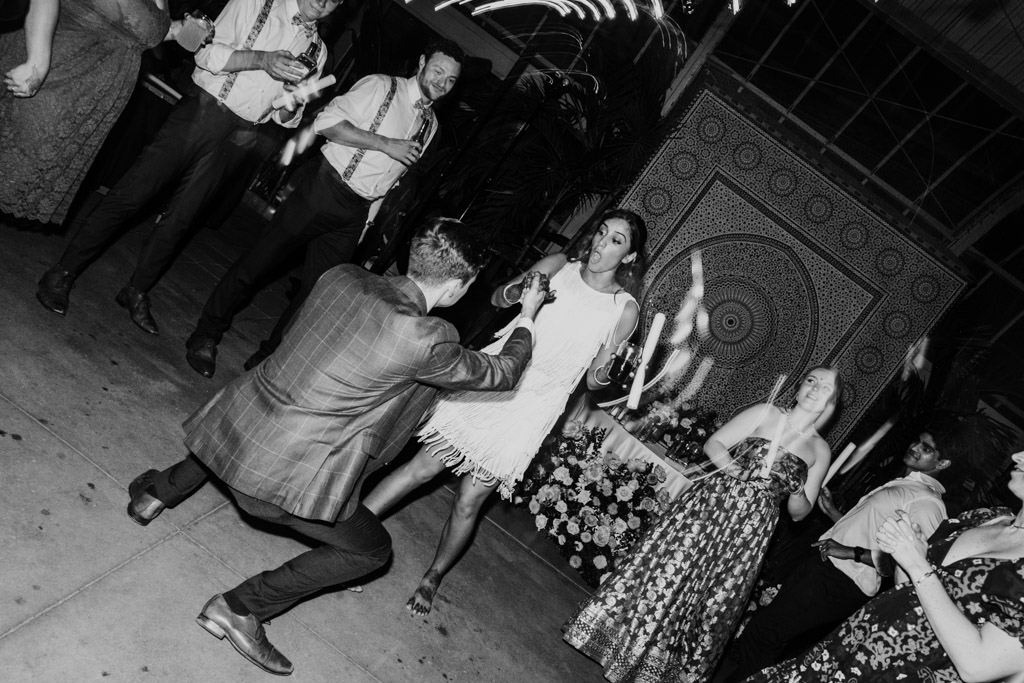 Black and white photo of bride and groom dancing at a lively Chicago Indian wedding, surrounded by cheering guests
