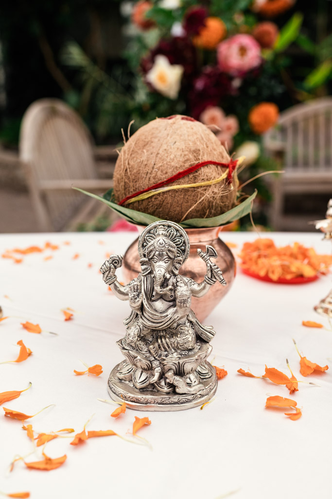Silver Ganesh idol with a coconut on a pot, surrounded by orange flower petals on a white table—an elegant decor element often seen at a traditional Chicago Indian wedding.