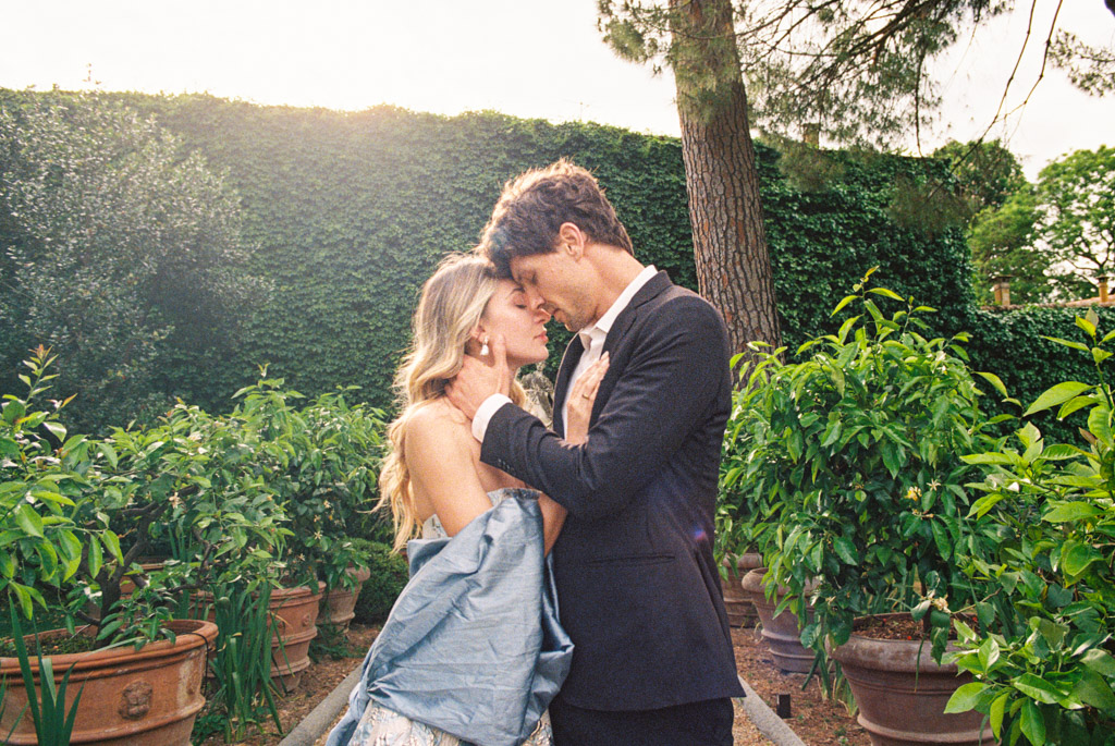 Engaged couple stands close together in Lucca Botanical Garden, embracing