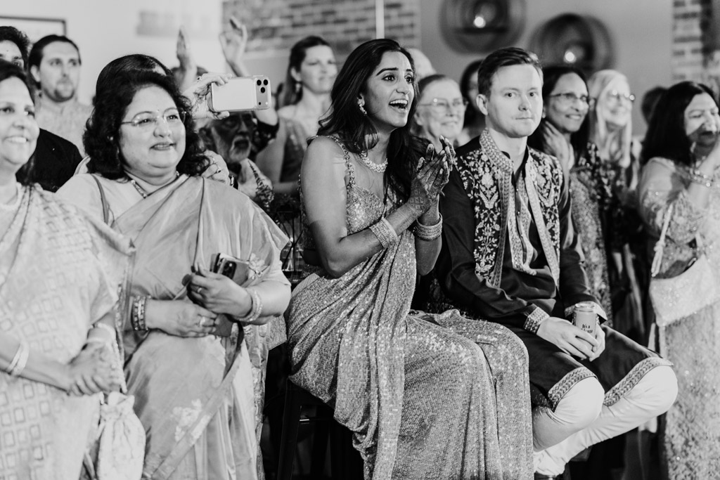 Black and white photo of bride, groom and guests in festive attire sitting and smiling during Sangeet at Ovation Chicago
