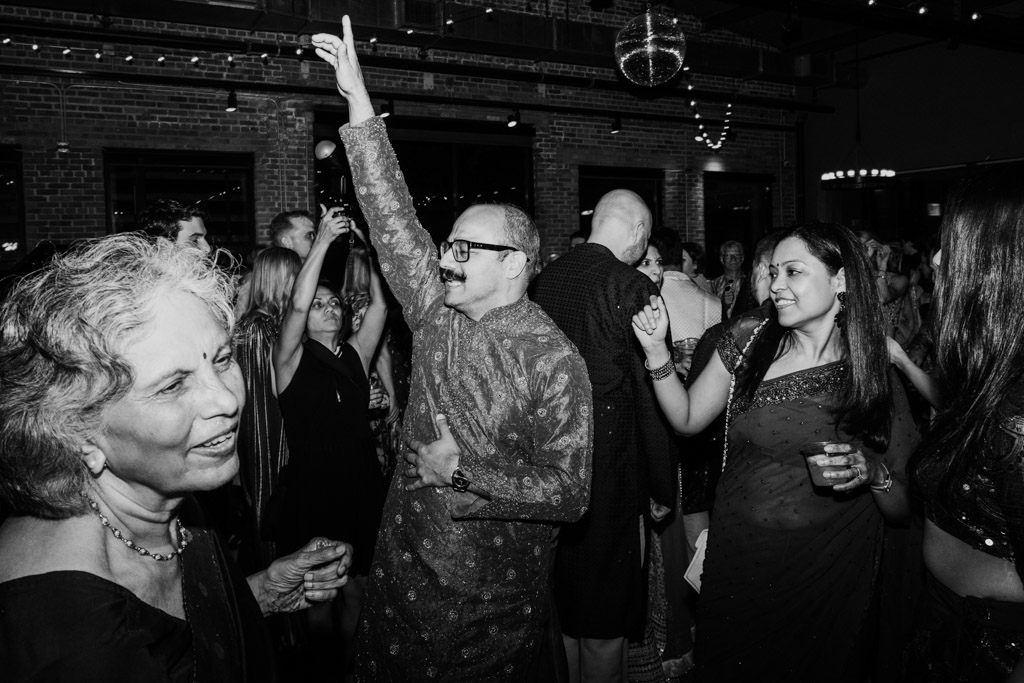 People in traditional attire dance and celebrate at a lively Chicago Sangeet indoor party, smiling and enjoying themselves.