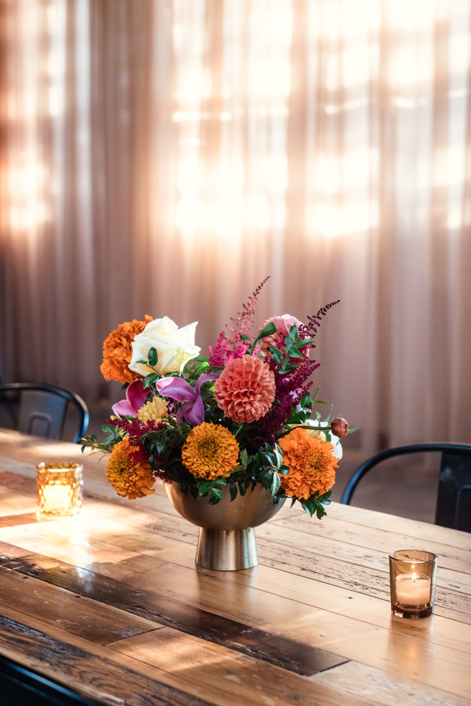 A gold vase with colorful flowers on a wooden table, surrounded by lit candle holders for Sangeet celebration at Ovation Chicago