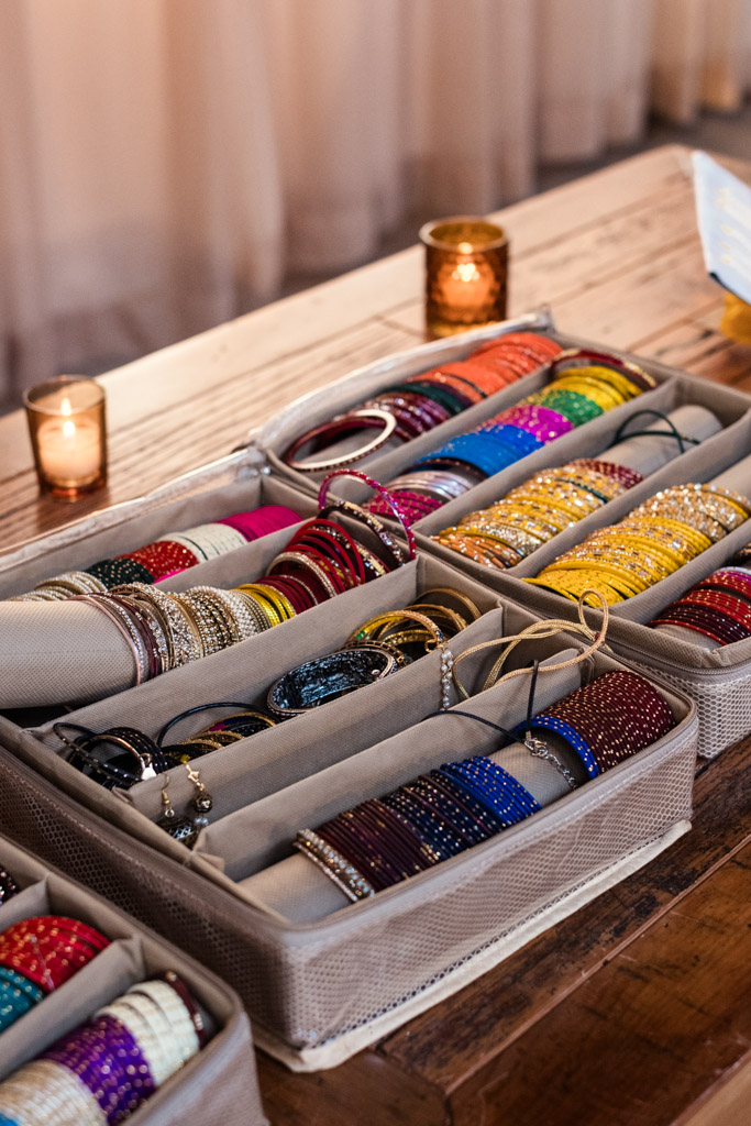 A jewelry box with colorful bangles organized in rows, placed on a wooden table with candles nearby for Sangeet celebration at Ovation Chicago