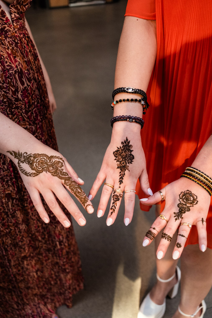 Two people showing intricate henna designs on their hands during a vibrant Sangeet at Ovation Chicago, wearing colorful dresses and jewelry
