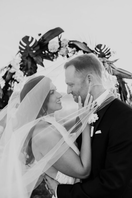 A bride and groom looking at each other under a shared wedding veil.