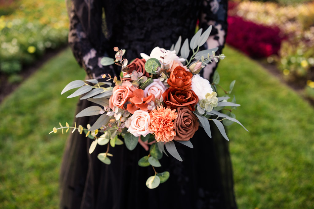 A person in a black dress holding a bouquet of rust-colored, peach, and white flowers with eucalyptus leaves.