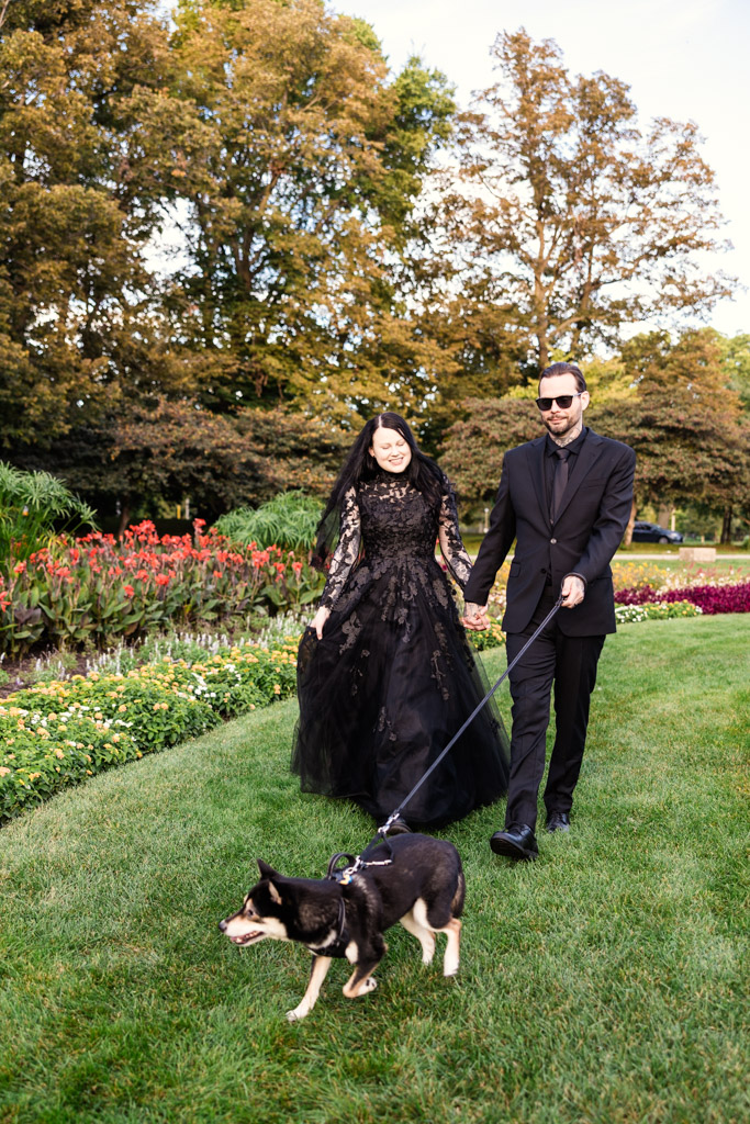A couple dressed in black walking a dog on a leash in a park.