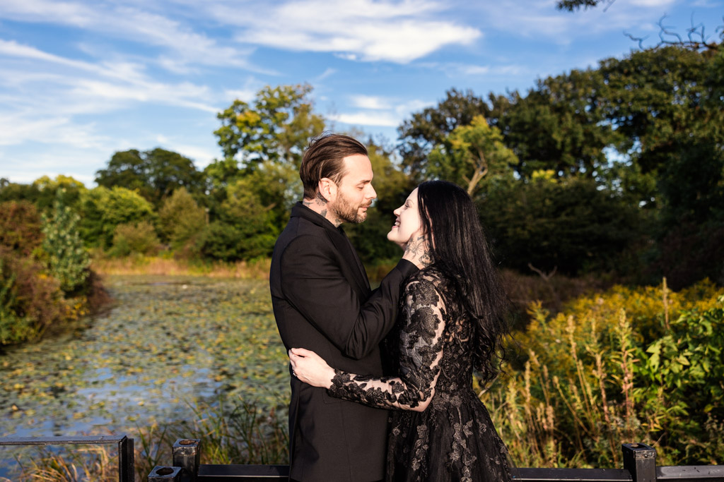 A couple in black formal wear embracing near a pond in a park.